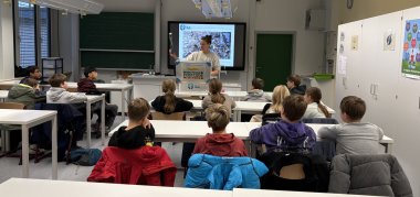 Zu sehen ist ein Klassenraum in dem die Kinder einer Präsentation zu hören