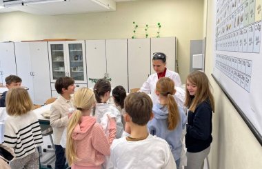 Vorstellung des Fachs Chemie Zu sehen sind mehrere Kinder die um eine Lehrerin herumstehen.