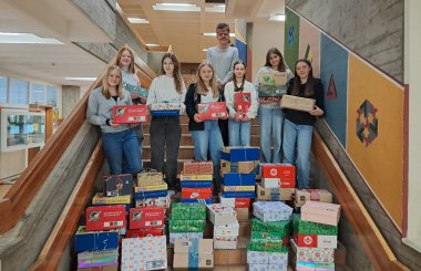 Zu sehen sind Emilia S., Lea F., Luisa K., Sara G., Josefina S., Dascha S., Leonie G. und Adrian J.. Vor ihnen stehen die ganzen gesammelten Kartons, eingepackt in Geschenkpapier.