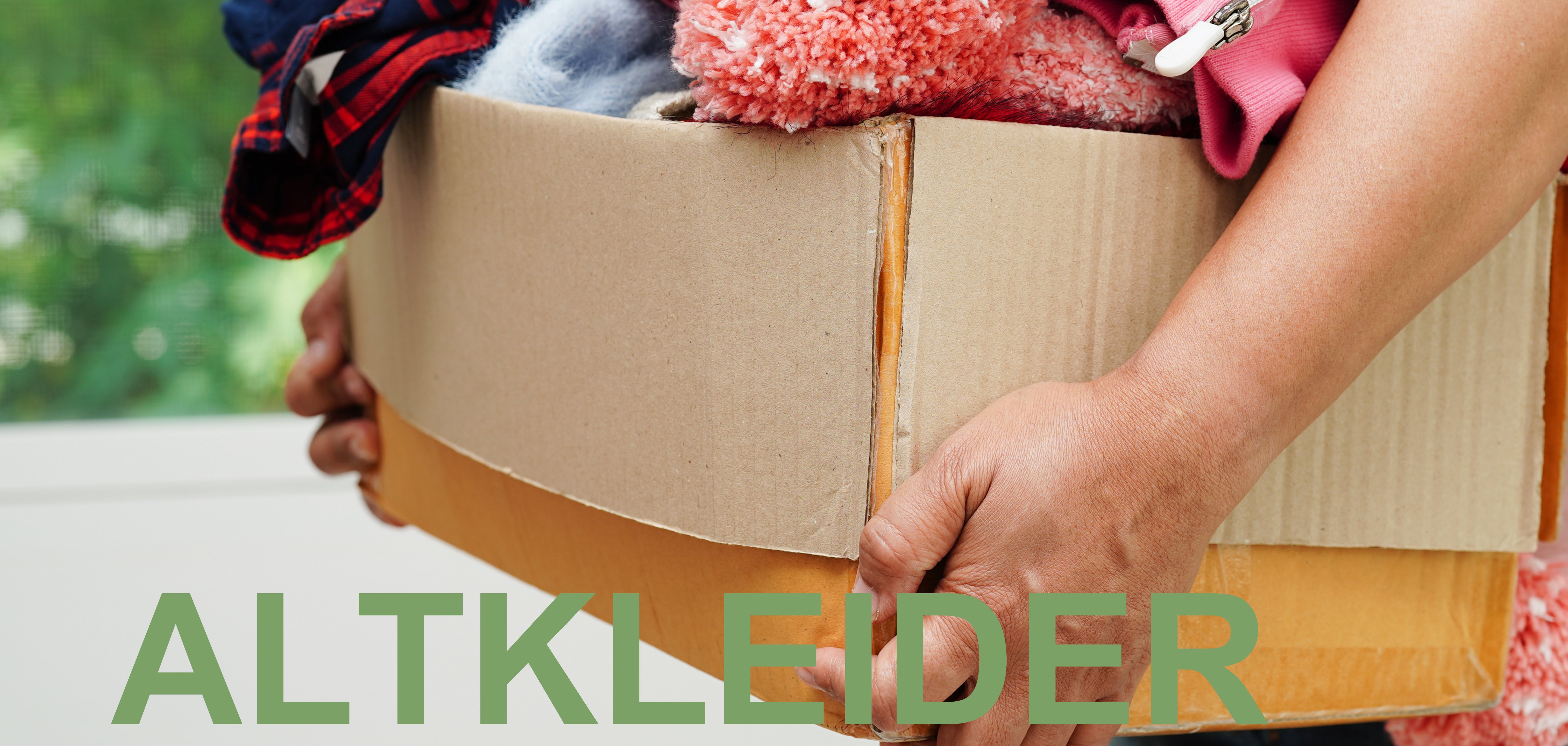 Karton mit Altkleidern, von einem Menschen getragen, nur die Arme sind sichtbar.