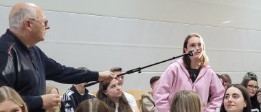 Austausch mit Politikern Zu sehen ist ein älter aussehender Mann der ein Mikrofon in der Hand hält. In das Mikrofon spricht eine Schülerin.
