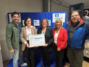 IGS Zell ist anerkannte UNESCO-Projektschule Zu sehen sind mehrere Personen die vor einem Aufsteller mit UNESCO Bildern stehen. Auf dem Bild sind Bildungsminister Sven Teuber (links), Frau Konrektorin Sabine Hayer, Schulleiterin Elke Raetz, Landrätin Anke Beilstein sowie der UNESCO Landeskoordinator Matthias Erlei (rechts)