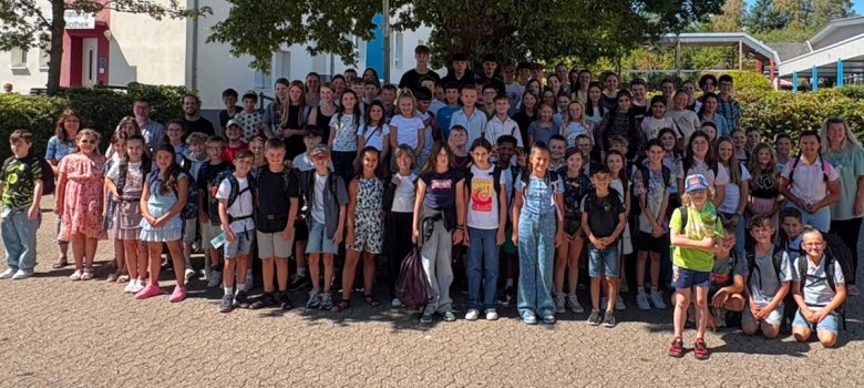 Einschulungsfeier neue Fünftklässler Das Bild zeigt die neuen Schülerinnen und Schüler der fünften Klassen. Sie stehen in einer großen Gruppe auf dem Schulhof im Schatten eines großen Baumes.
