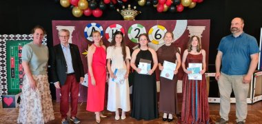 Abschlussfeier an der Realschule plus Vulkaneifel Zu sehen sind 8 Personen vor einem Dekoaufsteller der Abschlussfeier. Von links nach rechts sind folgende Personen zu sehen: Frau Nadine Fresia (Konrektorin der Realschule), Herr Siegfried Niederelz, Frau Hofmann (Lehrerin der Realschule), vier Schülerinnen, Herr Thorsten Künster (Didaktischer Koordinator).