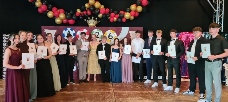 Abschlussfeier an der Realschule plus Vulkaneifel Zu sehen sind Schülerinnen und Schüler auf der Bühne in festlicher Kleidung. Diese halten ihre Abschlusszeugnisse der zehnten Klasse in der Hand.