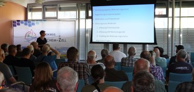 Erfolgreiche Schulung für die Kreisjägerschaft durchgeführt Dr. Kerstin Klug vom Veterinäramt des Landkreises Cochem-Zell schult über 110 aktiv Jagende der Kreisjägerschaft umfassend zur Digitalisierung in der Jagdpraxis. Das Foto ist im Sitzungssaal von hinten über die Zuhörerschaft hinweg nach vorne fotografiert. Dort steht Frau Dr. Klug und referiert. Neben ihr ist eine Landwand mit einer Präsentation zu sehen.