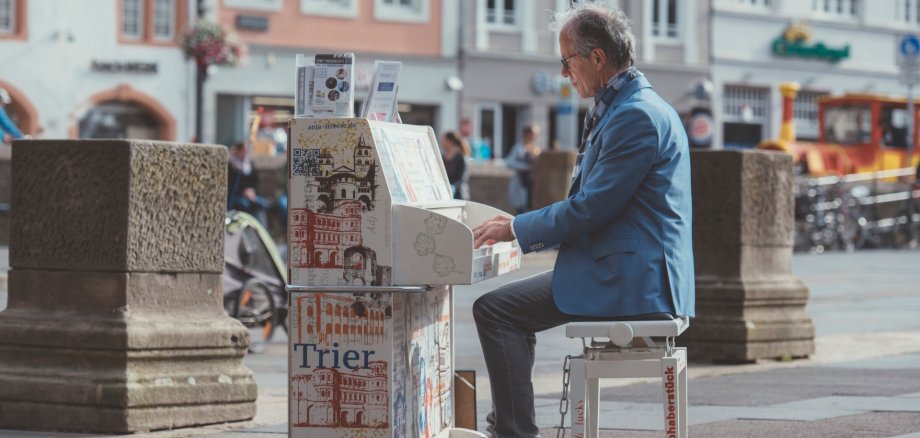 Mosel Musikfestival bringt „My Urban Piano“ im Juni auf die Marktplätze der Region – zuvor wird das Instrument gestaltet Zu sehen ist ein Mann, der an einem Klavier sitzt und spielt. Das Klavier steht dabei mitten auf einem Marktplatz.