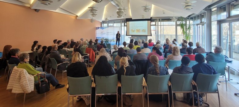 Großes Interesse an Vortrag zu Ernährung im Alter Großes Interesse an Vortrag zu Ernährung im Alter: Die Zuhörerinne und Zuhörer sitzen in Stuhlreihen im großen Sitzungssaal der Kreisverwaltung Cochem-Zell lauschen gespannt dem Vortrag von Referentin Theresa Lehnen, die vorn steht. Hinter ihr ist eine große Leinwand zu sehen, auf der die Präsentationsfolien angezeigt werden.