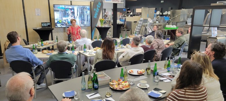 Tourismuscluster zu Gast bei der Fa. Wirtz in Zell: Kundenbegeisterung als Wachstumsstrategie Anne-Marie Vissers hat sich auf Kommunikation, Kundenservice und persönliche Entwicklung spezialisiert. Das Bild zeigt die Referentin bei Ihrem Vortrag zu Kundenbegeisterung und Customer Experience. Die Zuhörerinnen und Zuhörer sitzen im Halbkreis an Tischen und lauschen der Präsentation. Auf den Tischen stehen Getränke und Brötchen.