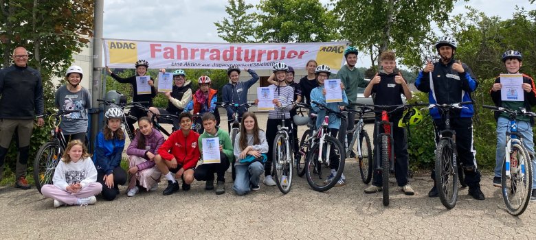 Realschule plus und FOS Kaisersesch beim ADAC Fahrradturnier: Das Gruppenbild zeigt Schülerinnen und Schüler, die - teils mit ihren Fahrrädern - gemeinsam mit ihrem Lehrer im Halbkreis unter einem Banner mit der Aufschrift "ADAC Fahrradtournier" aufgestellt sind. Einige halten Urkunden in die Kamera, andere zeigen einen Daumen hoch.
