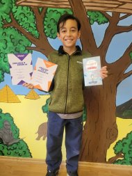 Aron Reif gewinnt Kreisentscheid Aron Reif gewinnt Kreisentscheid: Das Foto zeigt Aron Reif vor einer buten Wand. Er hält seine Urkunden in der Hand und lächelt.