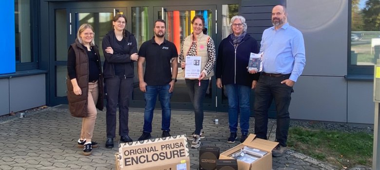 Moderne Technik für den Unterricht: Kampf GmbH spendet 3D-Drucker Das Foto zeigt sechs Personen (Vertreter und Vertreterinnen der Schule, der Firma Kampf sowie des Fördervereins) vor dem Eingang der Schule.