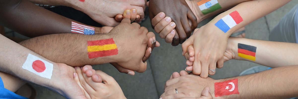 Menschen mit verschiedenen Hautfarben haben unterschiedlichen Flaggen auf ihren Armen gemalt und stehen miteinander im Kreis und halten sich die Hände. Menschen mit verschiedenen Hautfarben haben unterschiedlichen Flaggen auf ihren Armen gemalt und stehen miteinander im Kreis und halten sich die Hände.