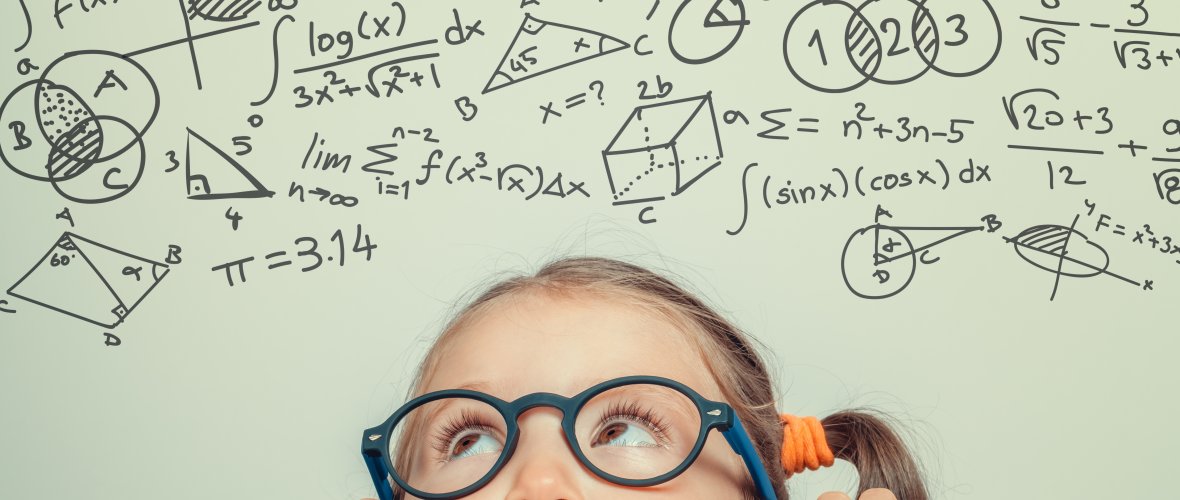 Ein kleines Kind mit einer schwarzen Brille schaut über den Rand eines Tisches auf viele Matheformeln.
