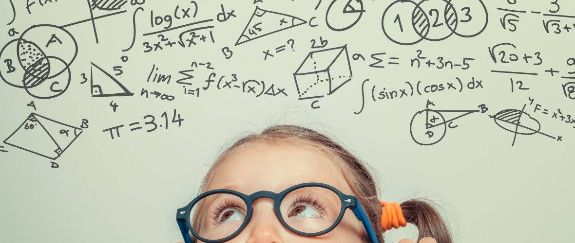 Ein kleines Kind mit einer schwarzen Brille schaut über den Rand eines Tisches auf viele Matheformeln. Ein kleines Kind mit einer schwarzen Brille schaut über den Rand eines Tisches auf viele Matheformeln.