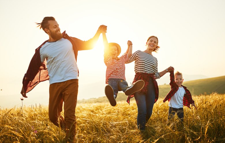Mutter, Vater und zwei Kinder gehen durch ein Feld bei Sonnenuntergang. 