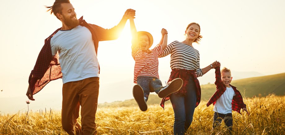Mutter, Vater und zwei Kinder gehen durch ein Feld bei Sonnenuntergang. 