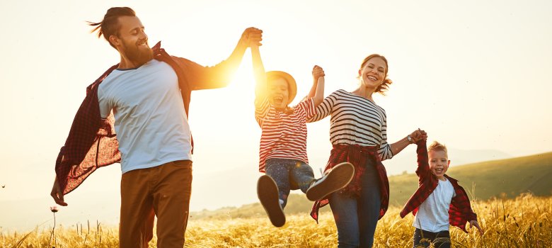 Mutter, Vater und zwei Kinder gehen durch ein Feld bei Sonnenuntergang. 