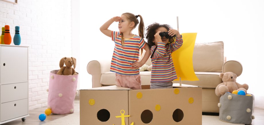 Cute little children playing with cardboard ship and binoculars at home