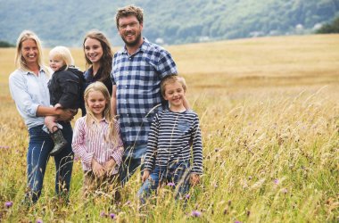 Familie mit 4 Kindern steht auf einer Wiese.