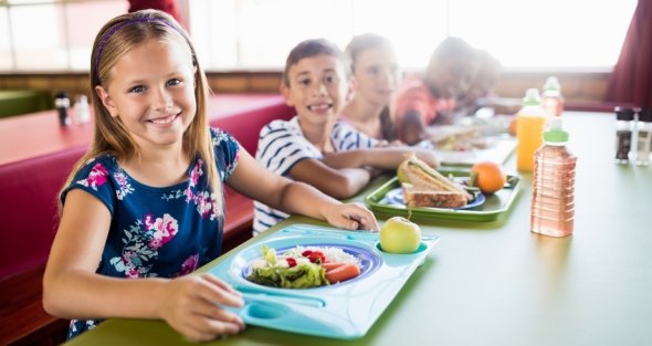 Dargestellt sind Kinder in einer Kantine, die ihr essen zu sich nehmen.