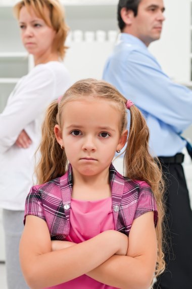 Konflikt in einer Familie, Mutter und Vater im Hintergrund, kleines Mädchen im Vordergrund mit verschränkten Armen.