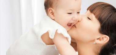 Dargestellt ist eine junge Frau, die ein Baby auf die Wange küsst.