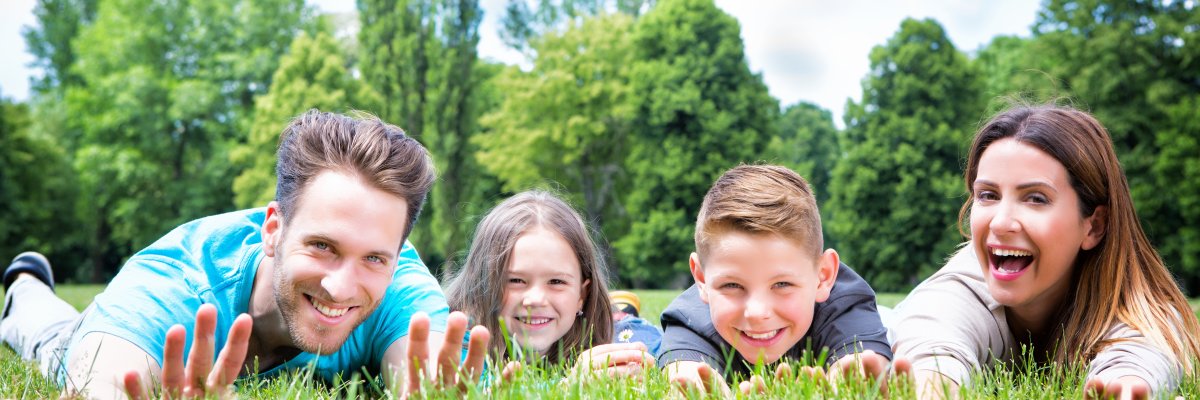 Familie aus Mutter, Vater und zwei Kindern liegen auf einer grünen Wiese.