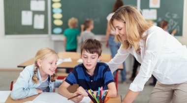 Dargestellt ist eine Lehrerin in einer Klasse mit zwei Kindern über ein paar Aufgaben.