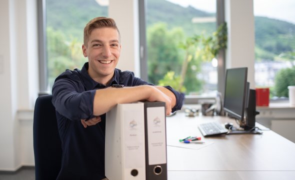 Ein Auszubildender stützt sich auf Aktenordner ab. Auf dem Bild werden mehrere Auszubildende der Kreisverwaltung dargestellt