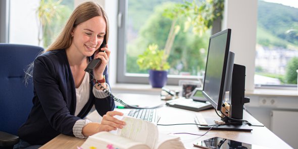 Eine Auszubildende sitzt an ihrem Schreibtisch und telefoniert. Dabei blättert sie in einem Gesetz. Zwei Auszubildende beim gemeinsamen Lernen