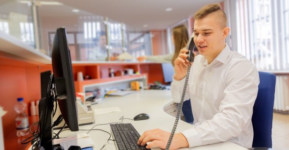 Ein Auszubildender sitzt an seinem Schreibtisch im Bürgerbüro und telefoniert. Zwei Auszubildende der Kreisverwaltung beim Lernen