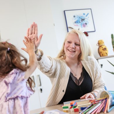 Sozialarbeiterin sitzt mit einem Kind am Tisch beim Spielen, beide schlagen ein. Sozialarbeiterin sitzt mit einem Kind am Tisch beim Spielen, beide schlagen ein.