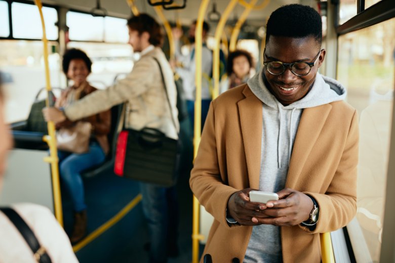 Junger glücklicher Mann liest SMS-Nachrichten auf Smartphone während der Reise mit dem Bus.