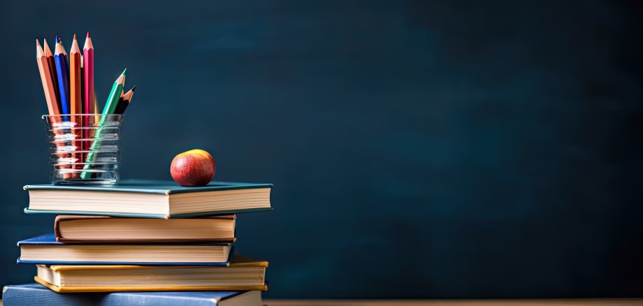 Stapel von Büchern und Bleistiften auf Schultisch vor dem Hintergrund der Tafel