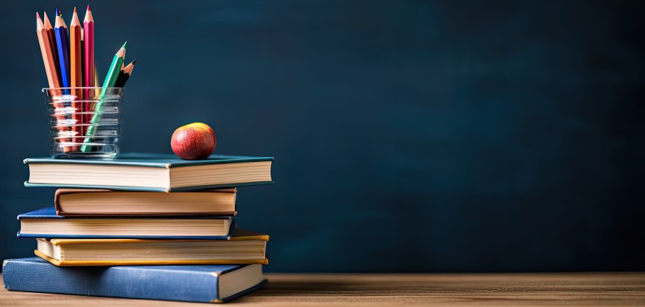 Stapel von Büchern und Bleistiften auf Schultisch vor dem Hintergrund der Tafel
