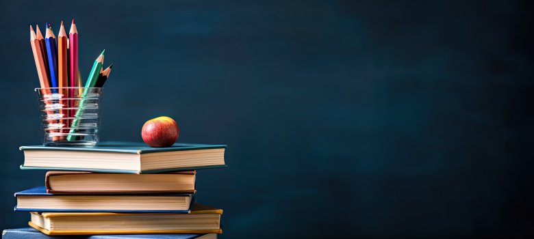 Stapel von Büchern und Bleistiften auf Schultisch vor dem Hintergrund der Tafel