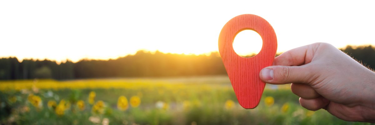 Eine Hand hält einen roten Positionsmarker im Sonnenuntergangshintergrund.  Eine Hand hält einen roten Positionsmarker im Sonnenuntergangshintergrund.