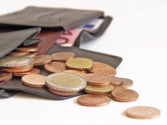 Dargestellt ist ein offenes Portmonee mit Kleingeld und eine 10 € Schein im Hintergrund.