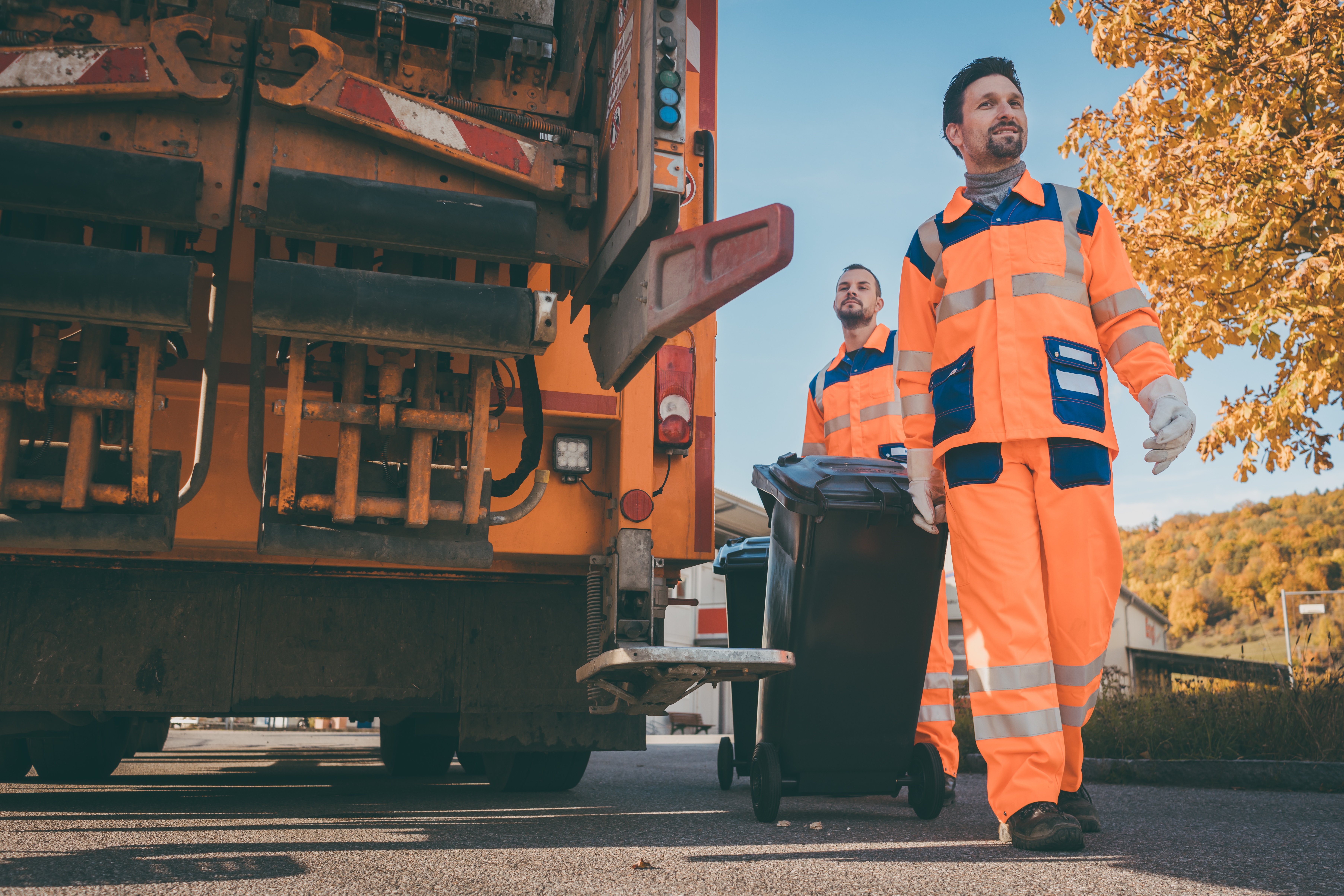 Two refuse collection workers loading garbage into waste truck