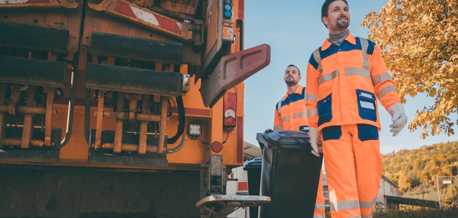 Two refuse collection workers loading garbage into waste truck