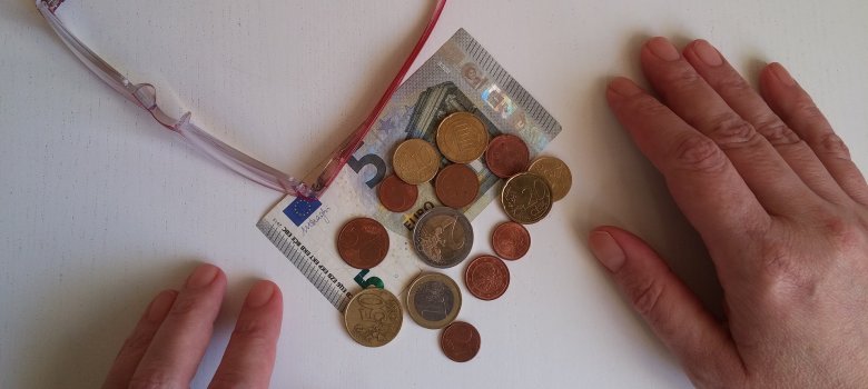 Zwei Hände und eine Brille umrahmen einen kleinen Berg an Kleingeld mit einem 5-€-Schein.